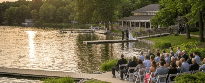 Outdoor lakeside wedding ceremony with guests seated by the water near a pavilion at sunset